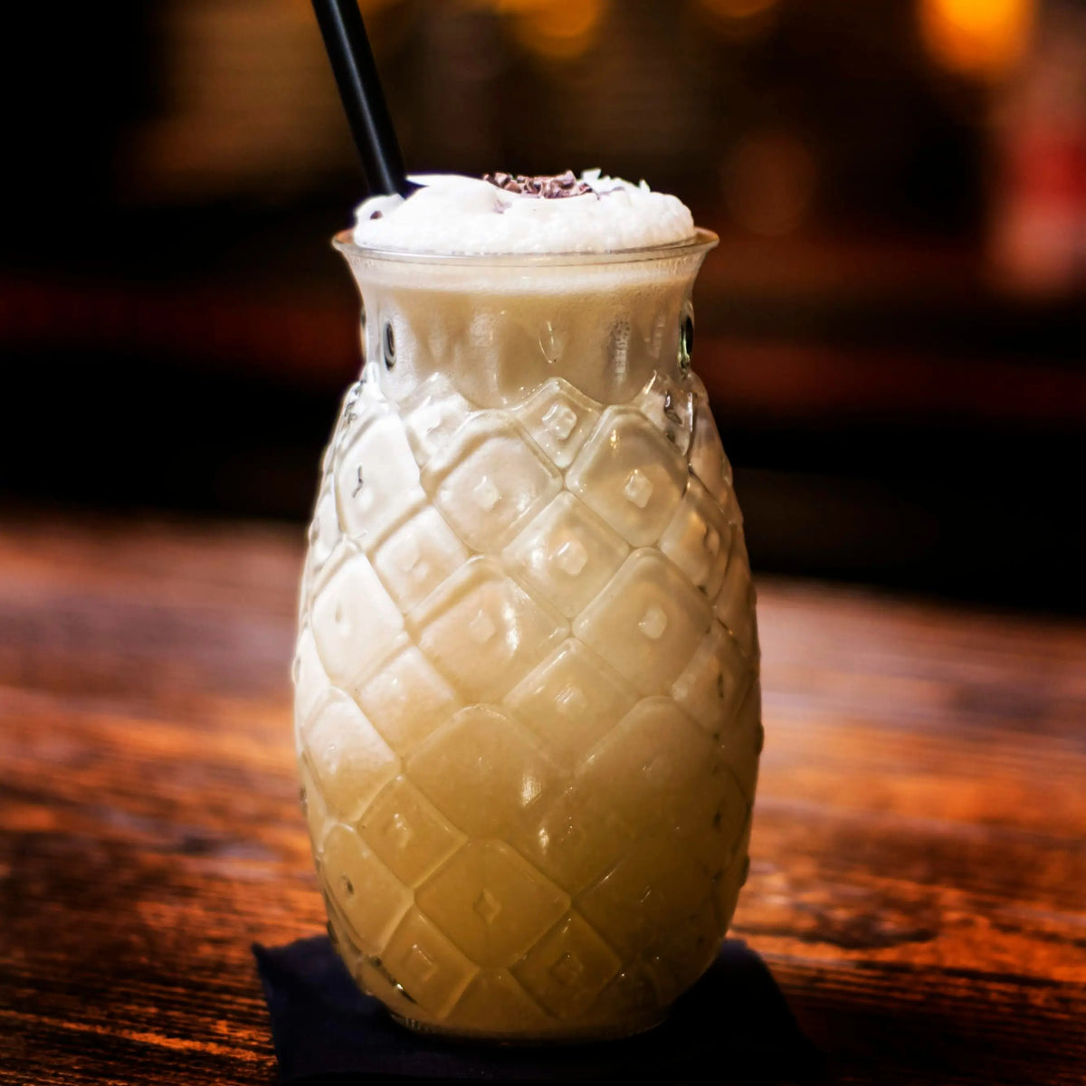 Koktajl Piña Colada podany w szkle w kształcie ananasa, na drewnianym blacie – egzotyczny drink na bazie kokosa i ananasa
