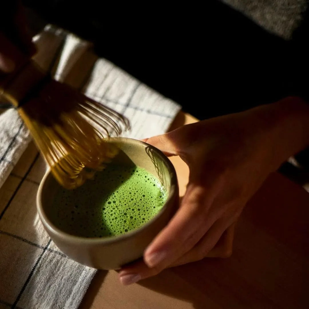 Przygotowanie matchy – ubijanie zielonej herbaty bambusową trzepaczką chasen w miseczce, rytuał parzenia matcha w naturalnym świetle