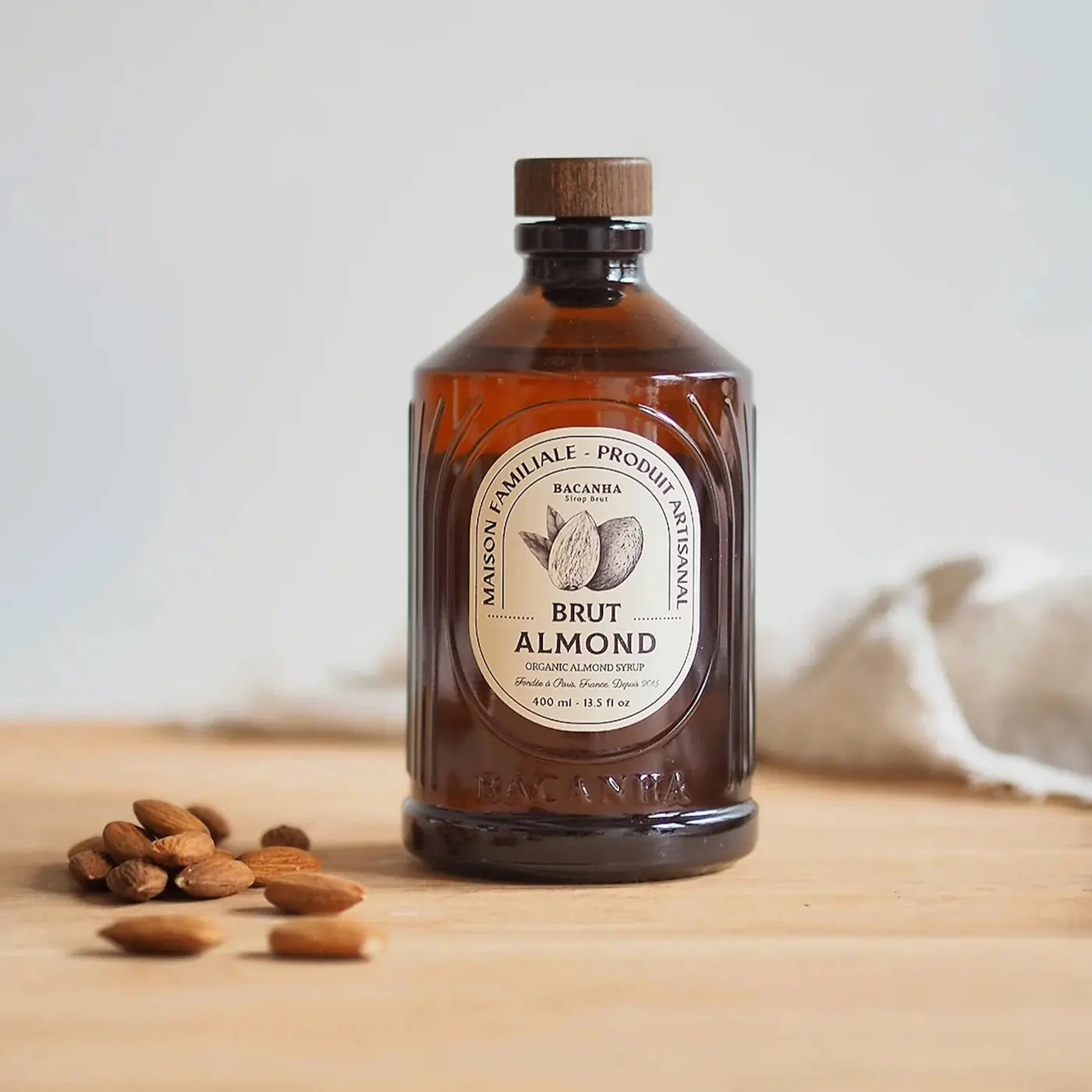 Butelka organicznego syropu migdałowego Bacanha Brut Almond trzymana w dłoni na drewnianym blacie.