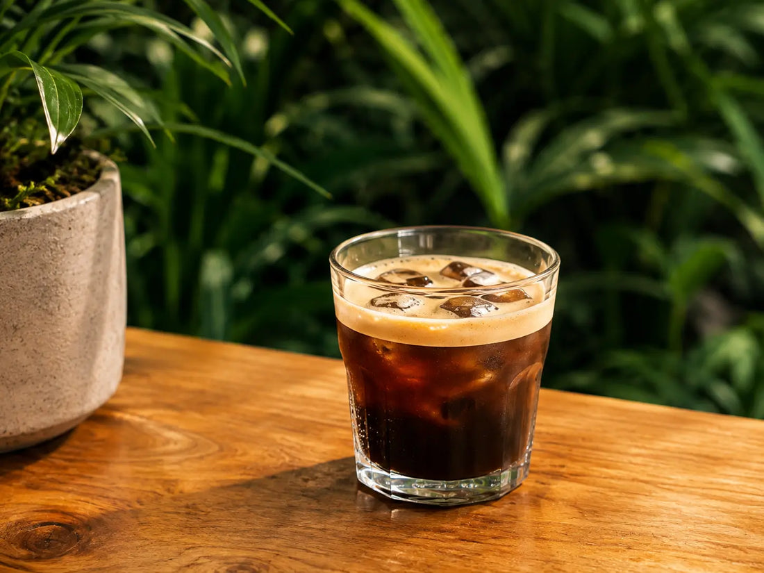 Freddo espresso w szklance z kremową pianką na drewnianym stole, w tle zielone rośliny doniczkowe
