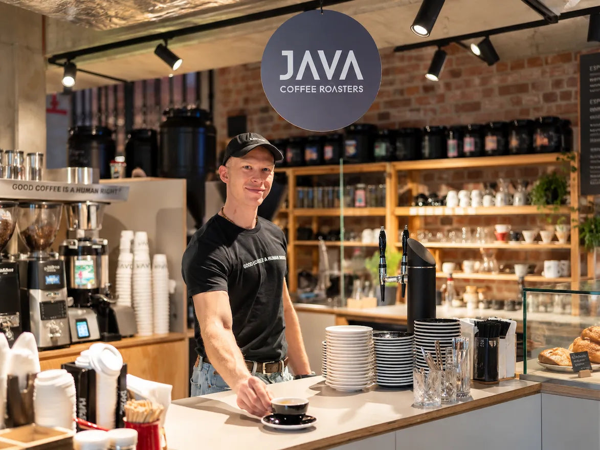 Barista JAVA Coffee Roasters podaje espresso przy barze kawowym wyposażonym w profesjonalny sprzęt.