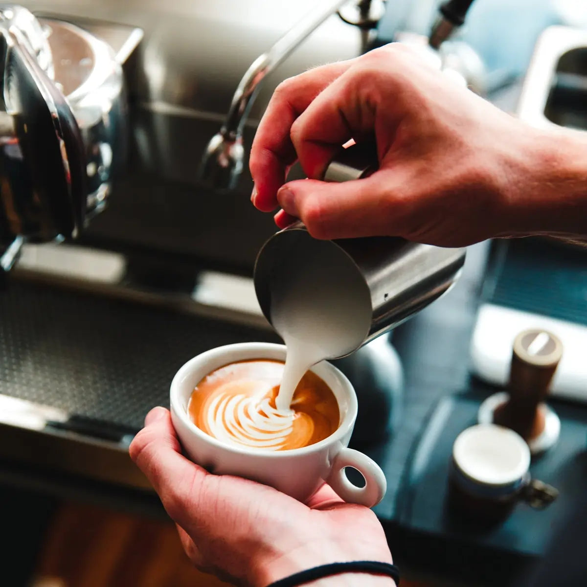 Barista wlewa spienione mleko do espresso – przygotowanie latte art w kawiarni.
