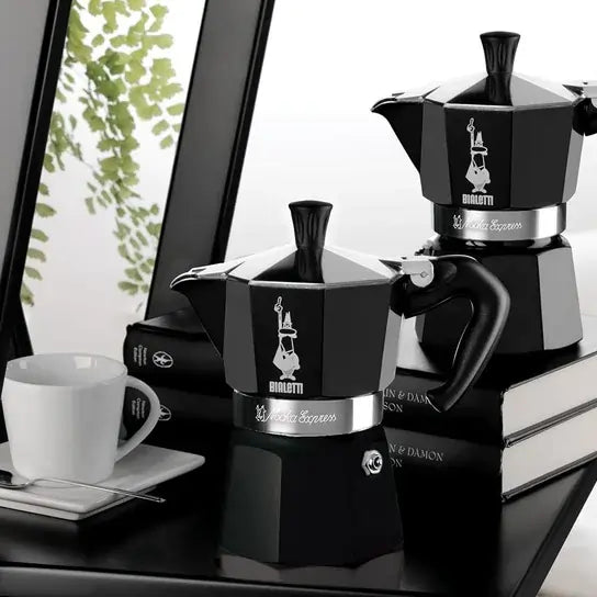 Czarna kawiarka Bialetti Moka Express 6 tz ustawiona na książkach w eleganckim wnętrzu – klasyczny design w matowej czerni z kontrastującym srebrnym wykończeniem.