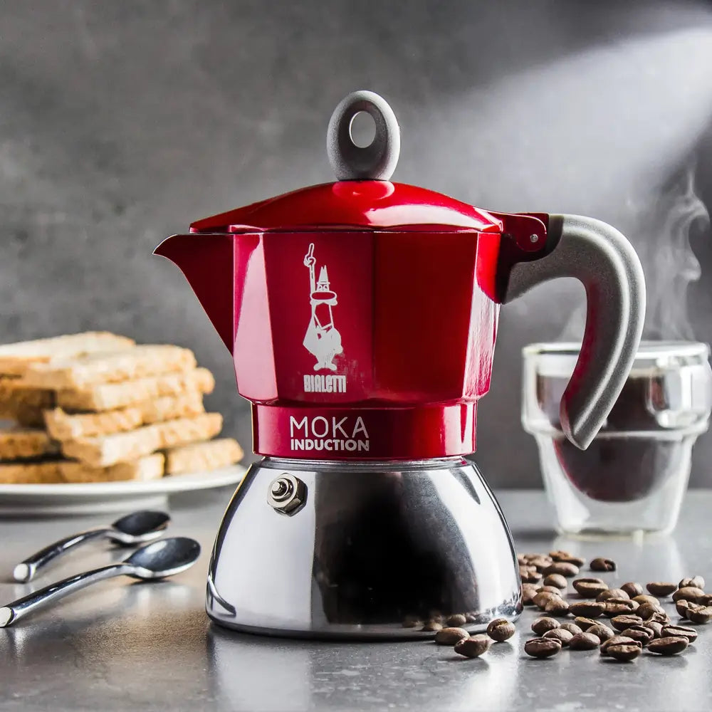 Czerwona kawiarka Bialetti Moka Induction podczas parzenia espresso, ziarna kawy i akcesoria w tle
