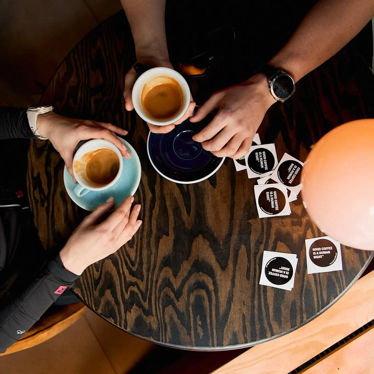 Dwie filiżanki espresso na drewnianym stole, naklejki JAVA z hasłem „Good coffee is a human right” i opakowanie kawy El Salvador