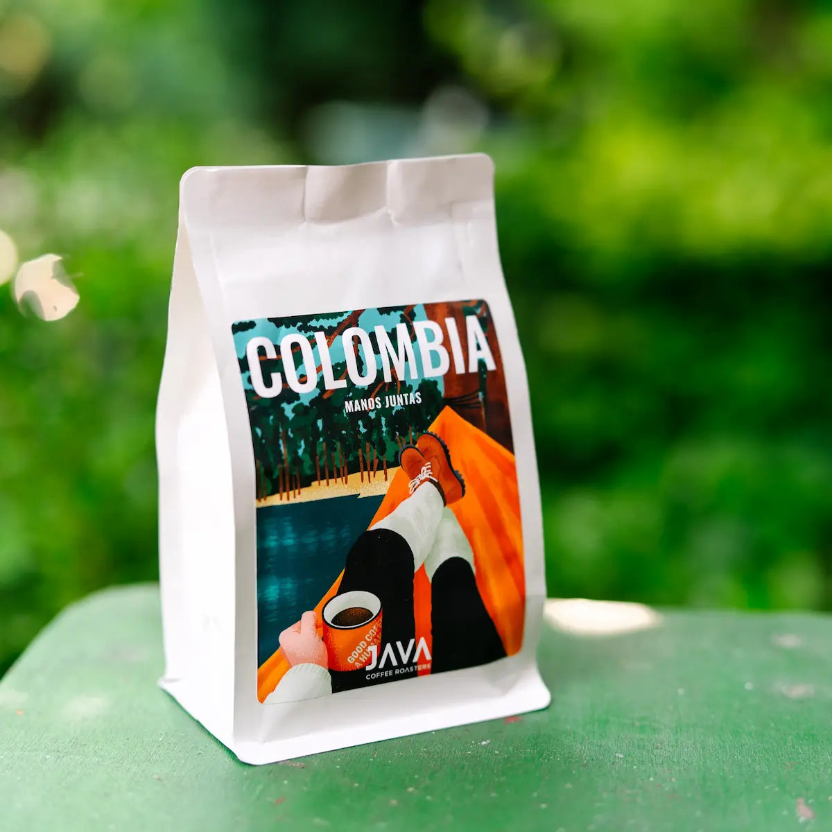 Opakowanie kawy specialty Colombia Manos Juntas od JAVA Coffee Roasters na tle zielonej natury.