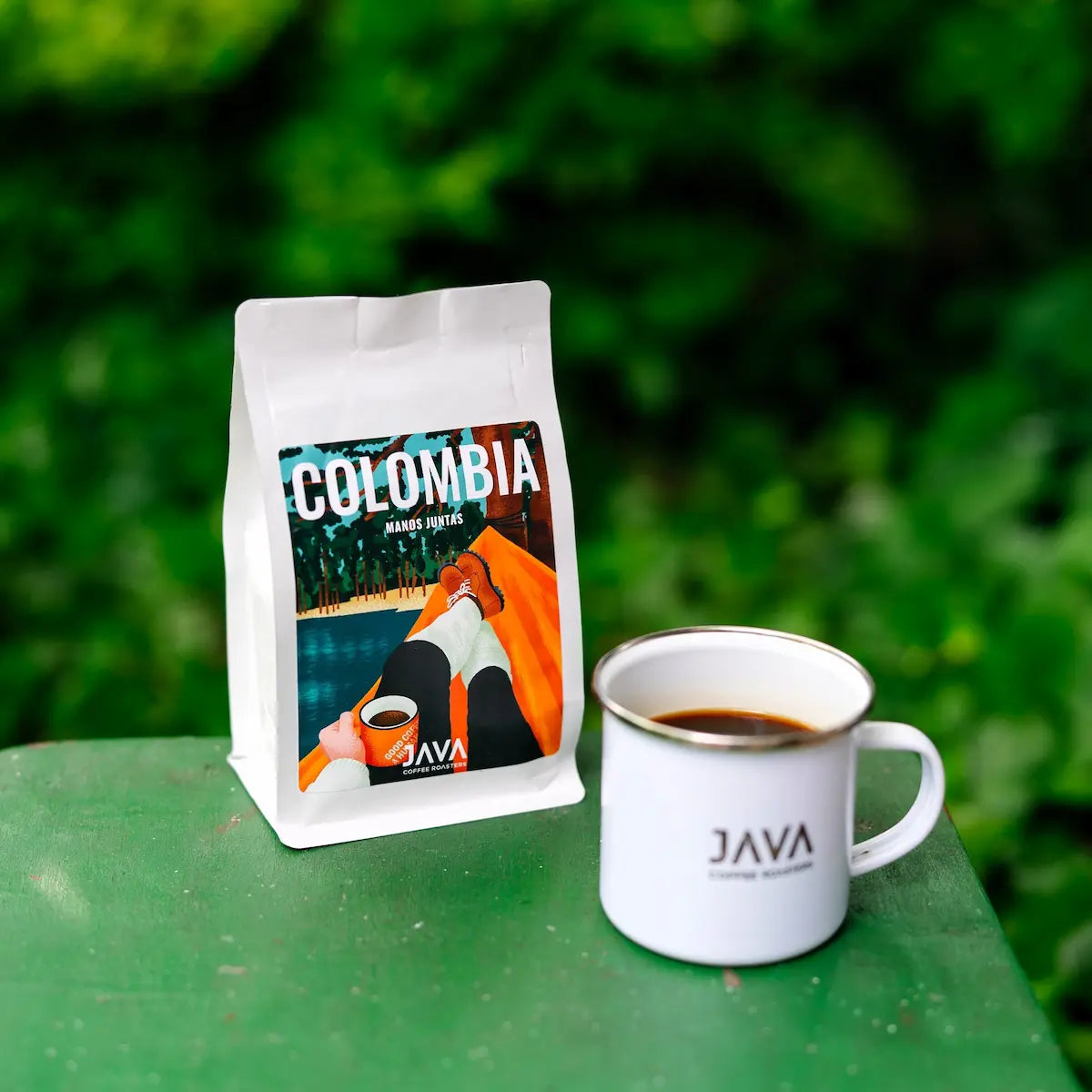 Kawa specialty Colombia Manos Juntas od JAVA Coffee Roasters z kubkiem świeżo zaparzonej kawy na tle zielonej natury.