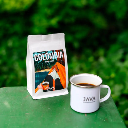 Kawa specialty Colombia Manos Juntas od JAVA Coffee Roasters z kubkiem świeżo zaparzonej kawy na tle zielonej natury.