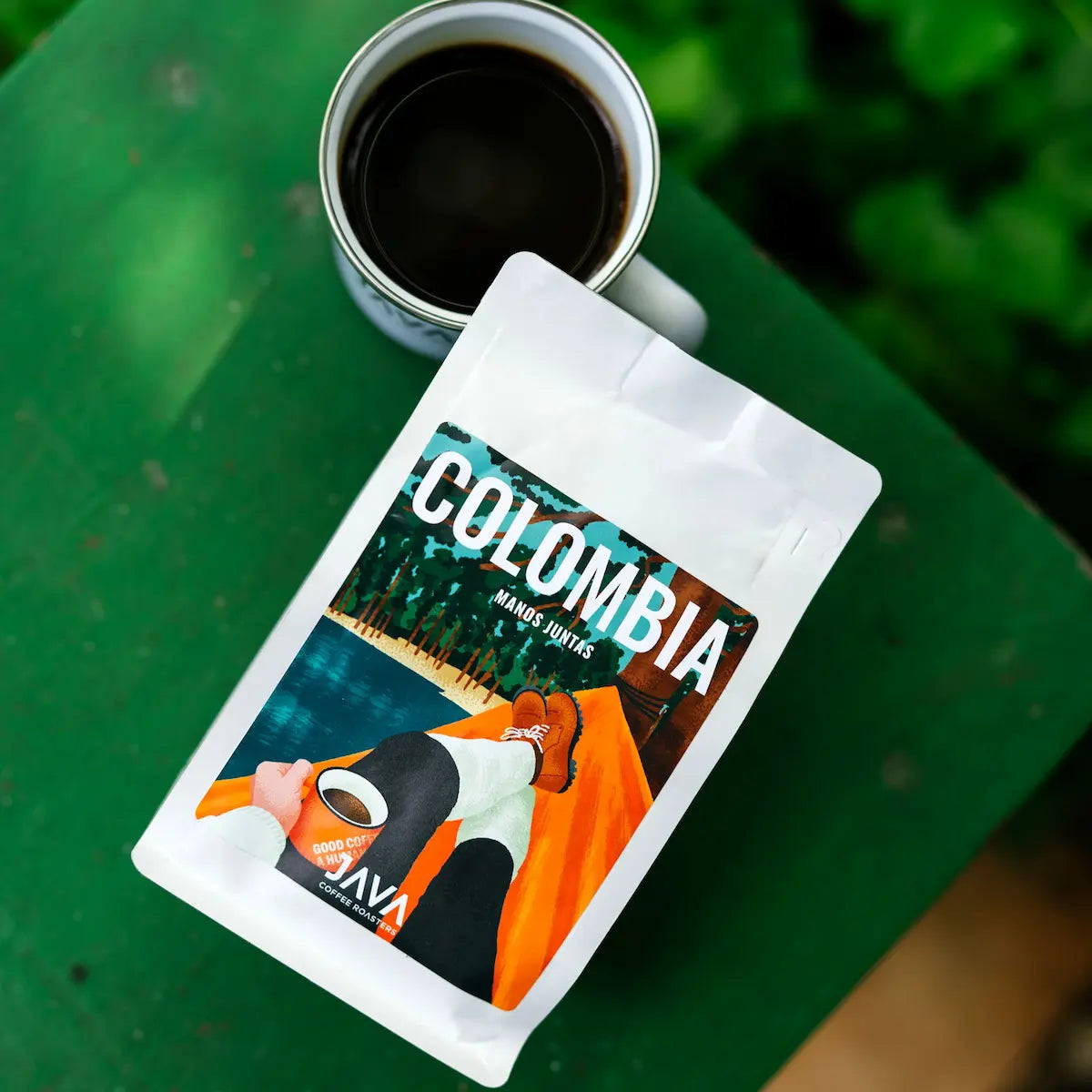 Kawa specialty Colombia Manos Juntas od JAVA Coffee Roasters z filiżanką świeżo zaparzonej kawy na tle natury.