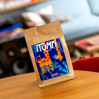 Kawa specialty Tanzania Itumpi od Java Coffee Roasters na drewnianym stole w nowoczesnym wnętrzu