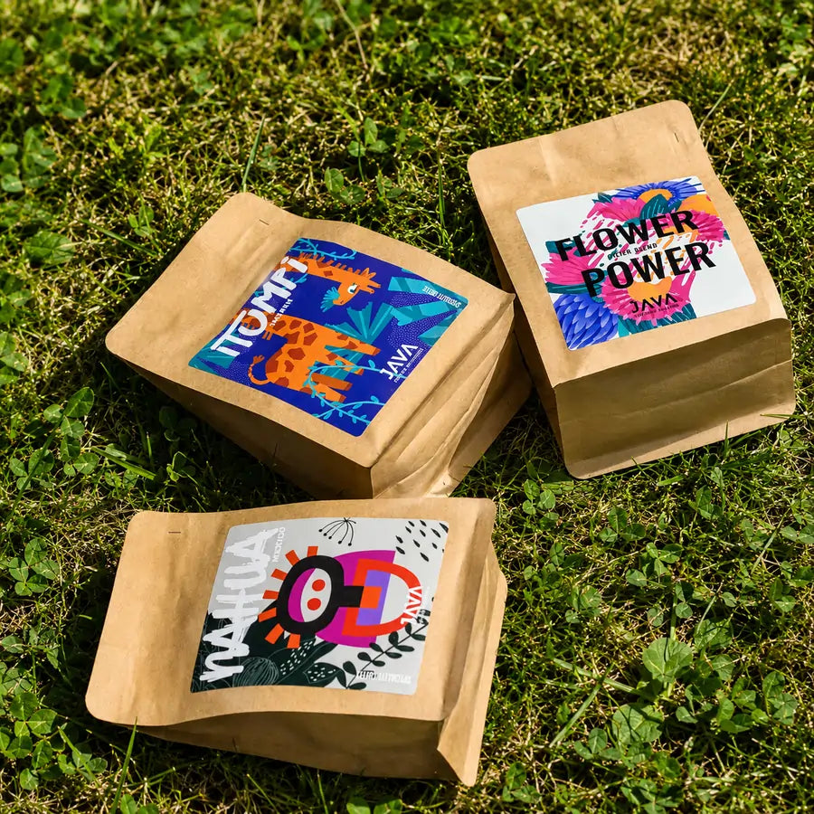 Kawy specialty JAVA Coffee Roasters – Flower Power, Nahua Mexico i Tanzania Itumpi ułożone na zielonej trawie podczas plenerowej sesji zdjęciowej .