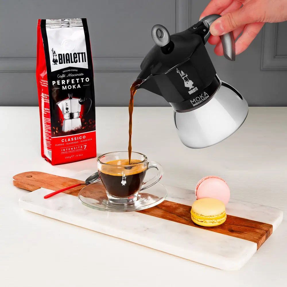 Kawiarka Bialetti Moka Induction w trakcie nalewania świeżo zaparzonej kawy do filiżanki, przygotowanie espresso w domowej kuchni, zdjęcie lifestyle