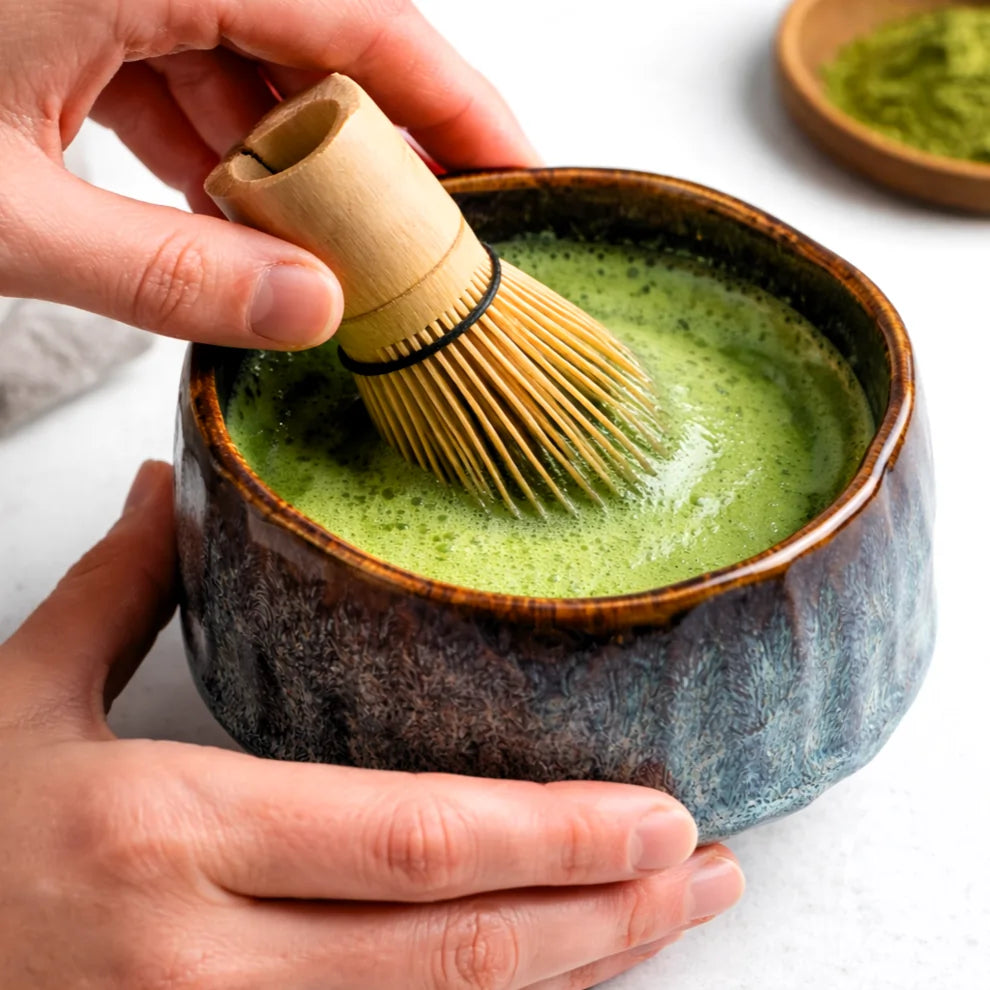 Ubijanie matchy bambusową miotełką chasen w ceramicznej czarce z niebiesko-brązową glazurą, proces przygotowania herbaty matcha.