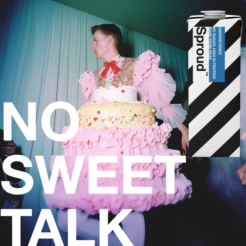 Karton Sproud Unsweetened obok osoby w teatralnej sukni w kształcie tortu – kampania napoju roślinnego bez cukru z hasłem „No sweet talk”.