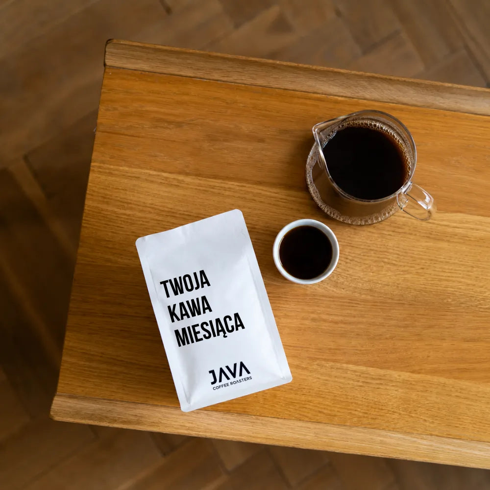 Subskrypcja kawy JAVA Coffee Warszawa – paczka Twoja Kawa Miesiąca z kawą przelewową i filiżanką na drewnianym stole