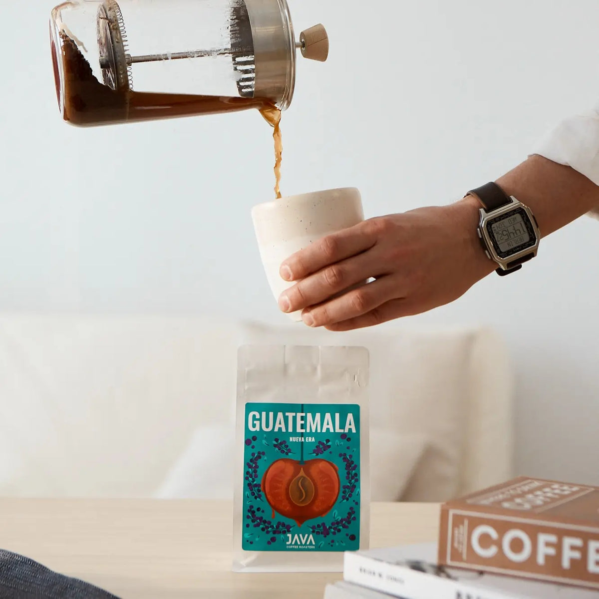 Parzenie kawy metodą French Press – kawa nalewana do filiżanki, w tle opakowanie kawy Specialty od JAVA Coffee Roasters.