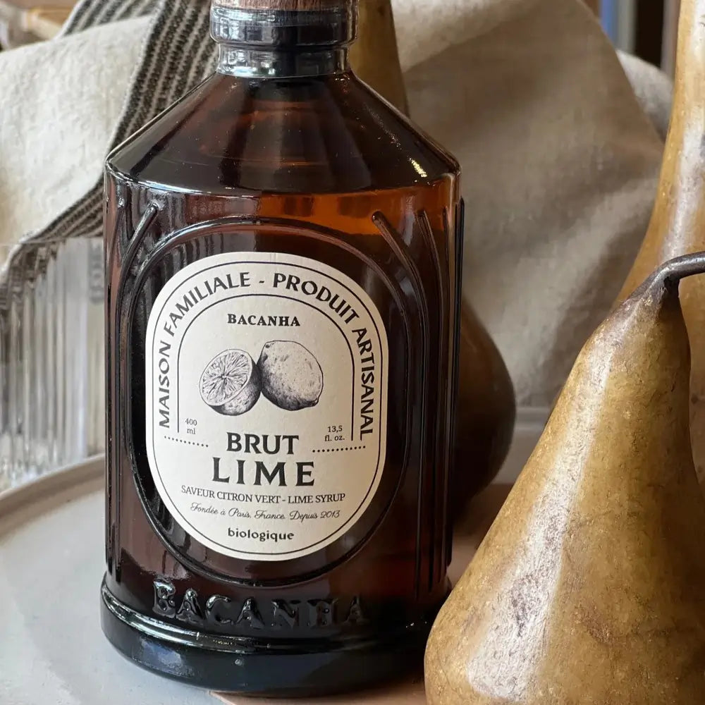 Syrop Bacanha o smaku limonki – organiczny syrop w bursztynowej butelce, ustawiony w stylowej aranżacji z gruszkami i tekstyliami