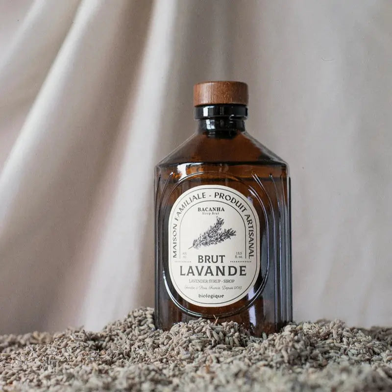 Butelka organicznego syropu Bacanha Brut Lavande na tle suszonej lawendy – naturalny syrop lawendowy do lemoniad, koktajli i deserów.