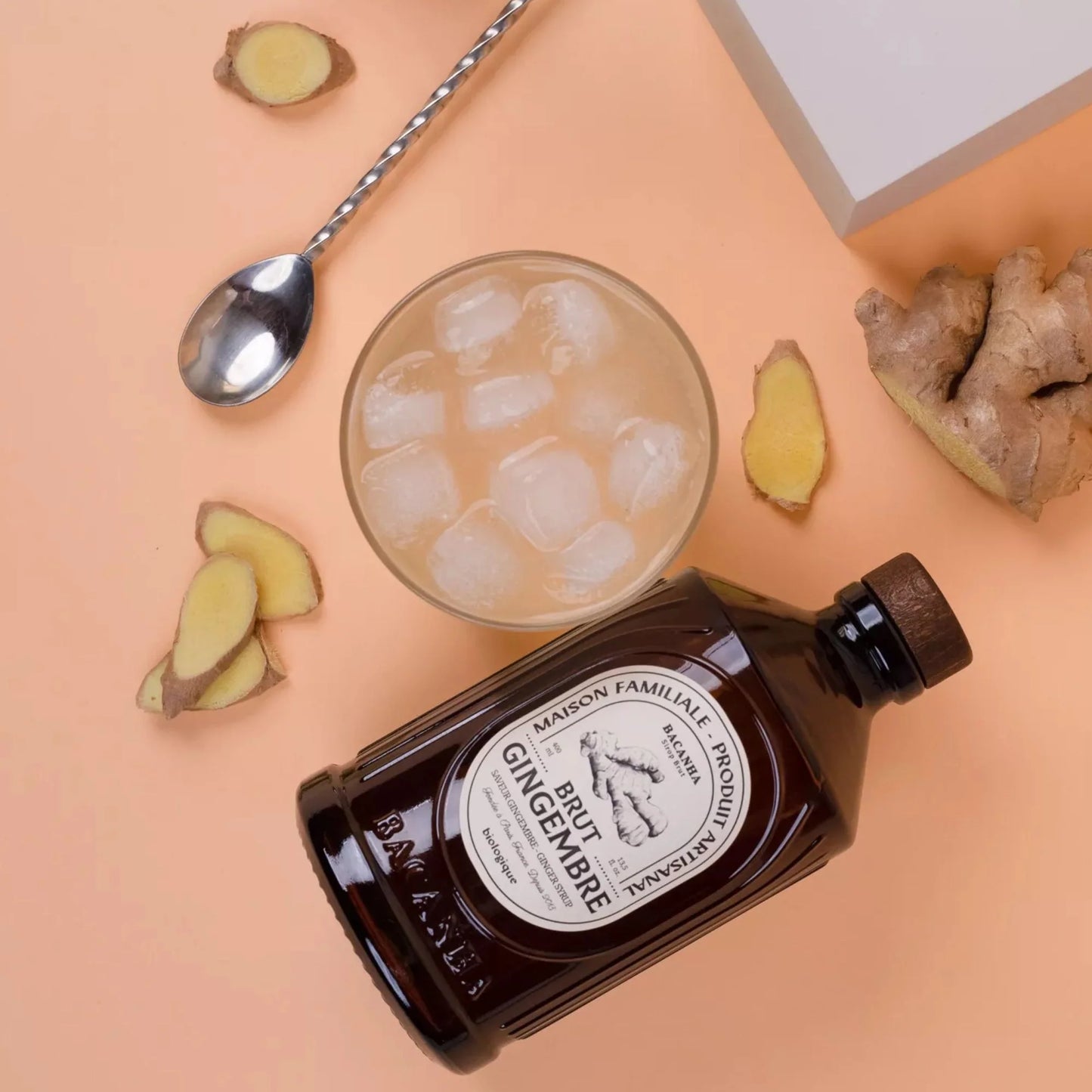 Syrop Bacanha Brut Gingembre (Imbirowy) z lodowym napojem i plasterkami świeżego imbiru – stylowa aranżacja na brzoskwiniowym tle.
