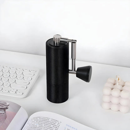 Ręczny młynek do kawy Timemore Chestnut C3s Pro Black ustawiony na biurku obok klawiatury, świeczki i otwartej książki – elegancki i minimalistyczny design